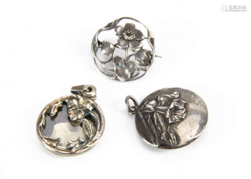 Three white metal floral Art Nouveau and Art Nouveau style pendants and brooches, comprising a