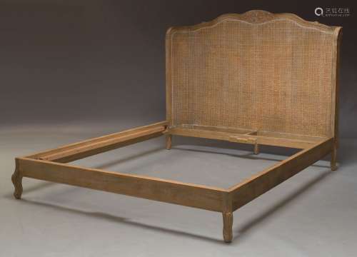 A limed wood and caned bed, of recent manufacture, the caned head board with carved floral