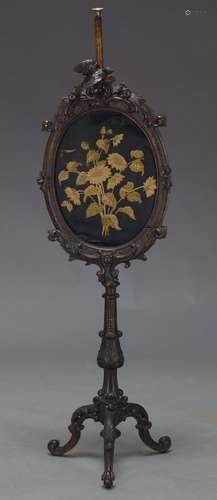 A Victorian mahogany fire screen, the oval frame with scrolling foliate decoration centred by carved