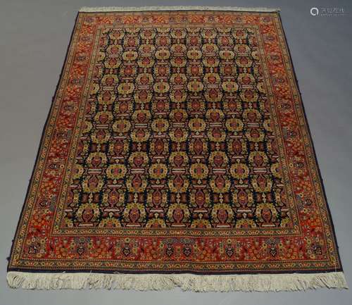 A Qum rug, late 20th Century, with repeat vase and floral spray pattern in indigo field, with red