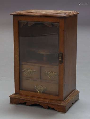 An Edwardian oak smoker's cabinet, with glazed door enclosing fitted interior and three drawers,
