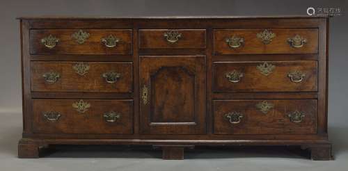 A George III oak dresser base, with seven drawers about a central cupboard door, raised on bracket