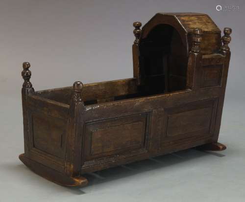 An oak rocking cot, late 17th, early 18th century, with hood and turned finials, above paneled