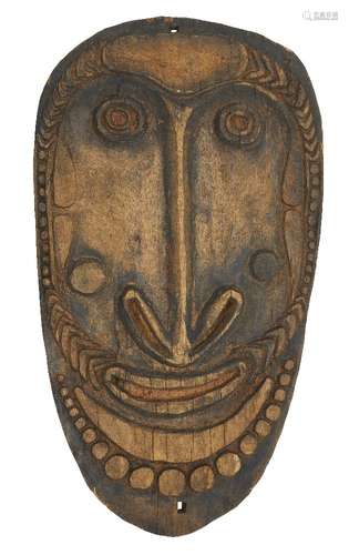 An oval tribal hardwood shield, 20th century, carved with a face within a beaded border, 95 x