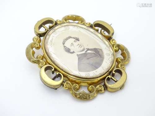 A Victorian brooch set with central rotating locket section within an ornate gilt metal C-scroll