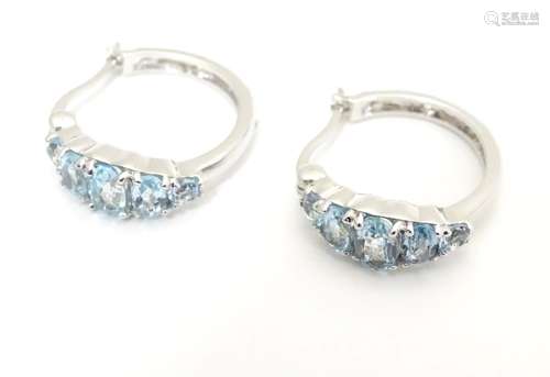 A pair of silver and white metal hoop earrings set with five graduated light blue stones. Stamped