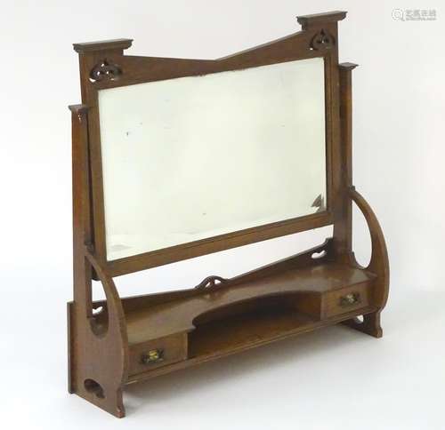 An early 20thC oak Art Nouveau table top dressing mirror with a decorative pierced frame, two