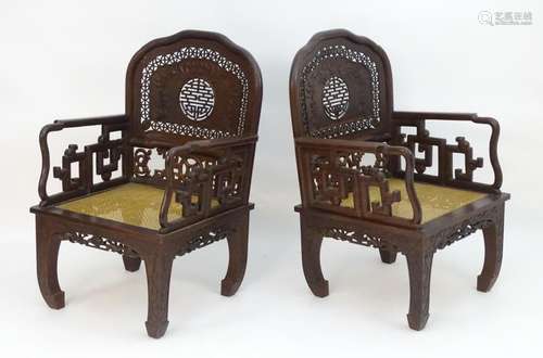 A pair of Chinese hardwood armchairs with pierced and carved backrests, fretwork supports and