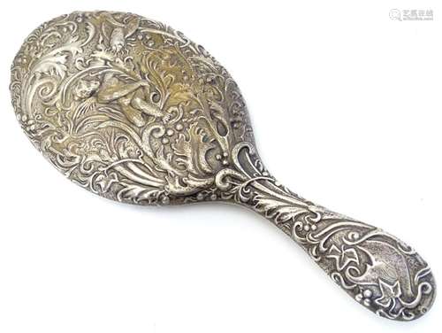 A silver hand mirror with embossed decoration depicting putto amongst foliage with winged insect.