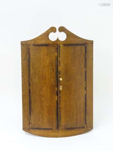 A late 18thC bowfronted oak corner cupboard with a swans neck pediment above mahogany crossbanded