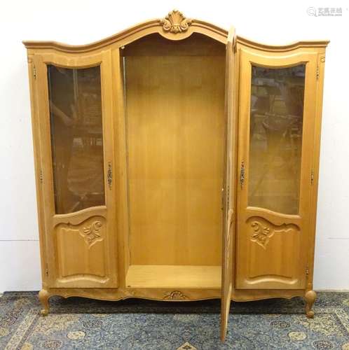 An early 20thC oak vitrine / armoire with a shell carved top and three glazed doors with carved