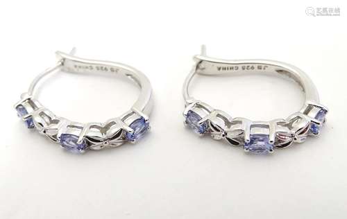 A pair of silver and white metal elongated hoop-like earrings set with three mauve stones. Stamped