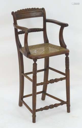 A 19thC walnut child's chair with a carved cresting rail, caned seat and standing on turned tapering