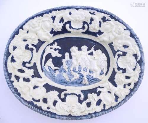 An Italian style charger of oval form with relief decoration depicting putti in a landscape. The