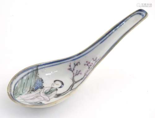 A Chinese famille rose soup spoon decorated with a figure in a landscape with a cherry blossom tree.