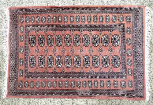 A salmon ground rug decorated with geometric banding and floral vignettes. Approx 60