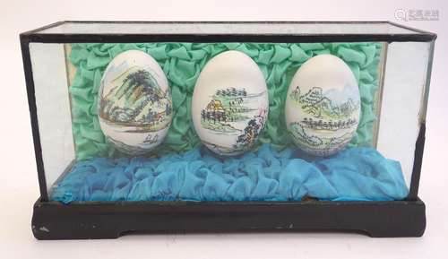 Three 20thC Chinese hand painted eggs depicting Oriental landscapes contained within a glazed