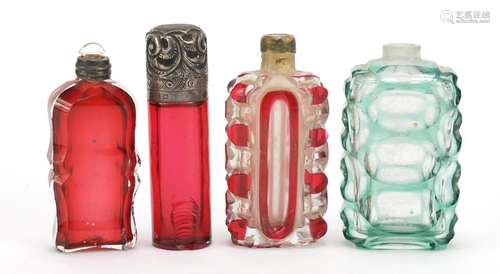 Four Victorian glass scent bottles including a cranberry example with embossed silver lid, the