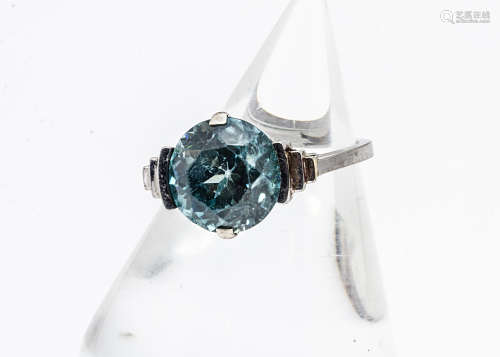 An Art Deco white metal zircon dress ring, the circular cut blue zircon in a four claw clamp setting