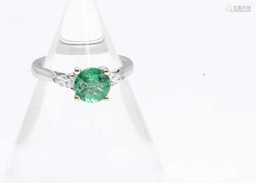 A contemporary emerald and diamond 18ct white gold three stone ring, the circular cut emerald in