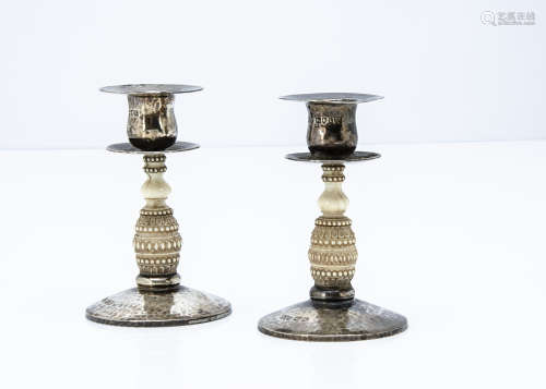 A pair of early George V silver and ivory candlesticks, circular hammer beaten bases with carved