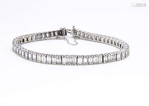 A diamond baguette cut 18ct gold tennis bracelet, the fifty eight claw set emerald cut stones in