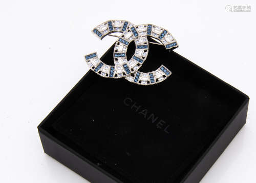 A paste set Chanel logo brooch, in blue and colourless step cut stones, with oval mark to base, in