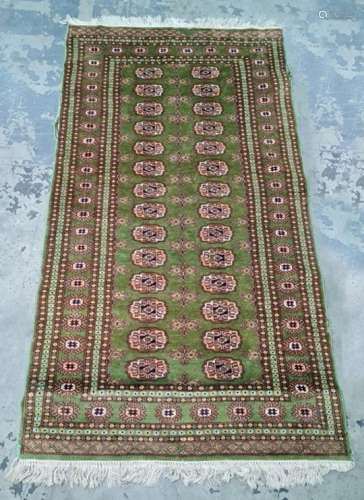 Green ground Persian rug with 28 elephant foot guls arranged across two rows, on a stepped border,