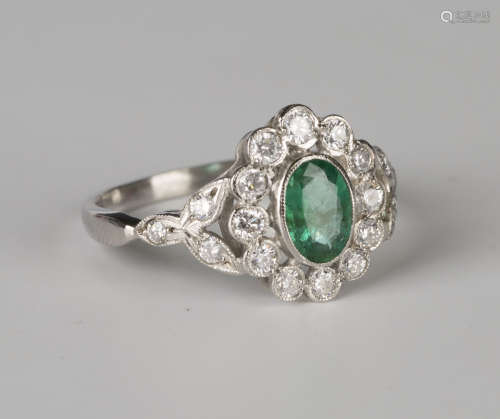 A platinum, emerald and diamond ring, collet set with an oval cut emerald within a surround of