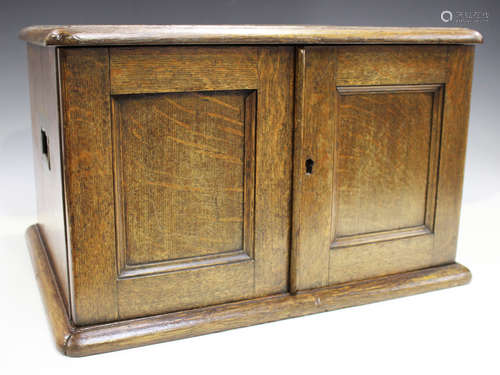 An Edwardian oak canteen box with a pair of panelled doors revealing four graduated drawers with