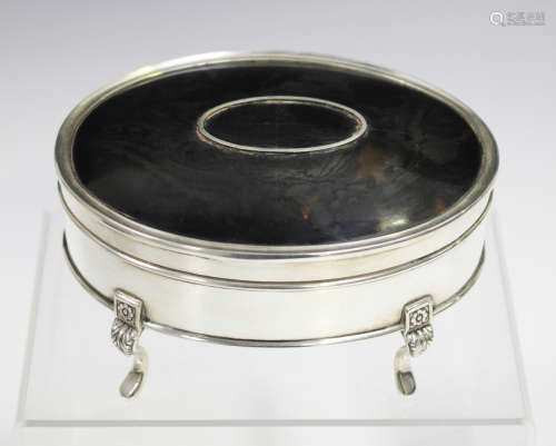 A George V silver oval jewellery box with inset tortoiseshell panelled hinged lid, raised on foliate