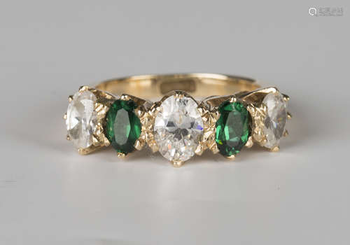 A gold ring, mounted with two oval cut green gems alternating with three larger oval cut