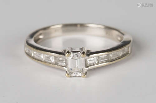 A white gold and diamond ring, claw set with the principal cut cornered rectangular emerald cut