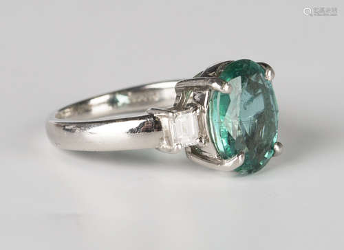 A platinum, emerald and diamond ring, claw set with an oval cut emerald between rectangular cut