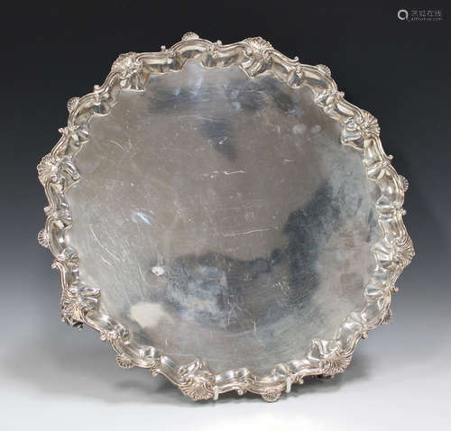 A large late Victorian silver salver with cast scroll and scalloped rim, raised on four volute