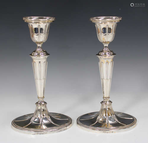 A pair of Edwardian silver candlesticks, each oval urn shaped sconce with beaded rim, above a