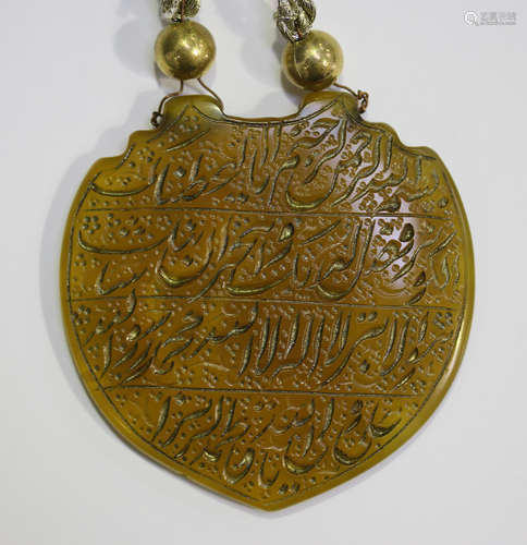 An Islamic yellow agate pendant of shield shape, finely incised and gilt with lines of script, width