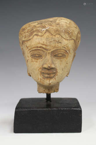 An Indonesian carved and painted wood head of a female deity, height 9.5cm, on an ebonized plinth.