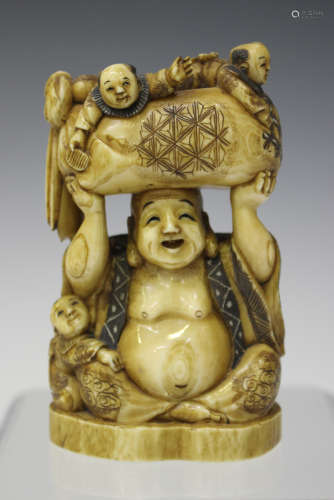 A Japanese carved and stained ivory okimono figure group, Meiji/Taisho period, modelled as Hotei