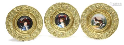 Three painted porcelain dishes in repousse brass frames, two with portraits of elegantly dressed