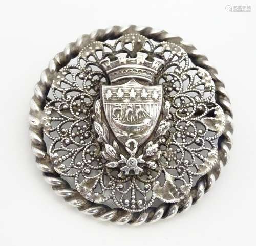 A white metal brooch of circular form with shield armorial to centre depicting Nordic long boat.