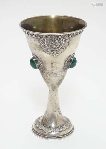 A Continental white metal chalice of conical form with gilded interior and set with three green/