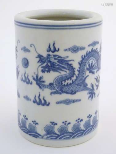 A Chinese blue and white cylindrical brush pot decorated with stylised dragons, clouds and flames.