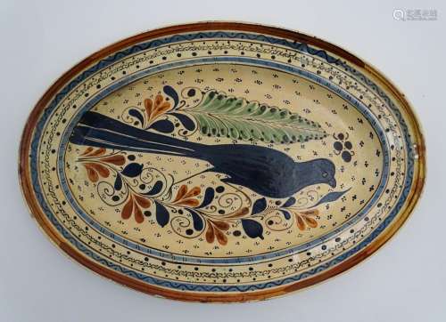 A Swiss terracotta oval pottery dish with hand painted folk art decoration depicting a bird