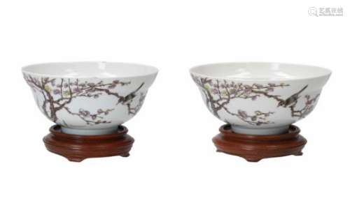 A pair of polychrome porcelain bowls on wooden stand, decorated with a bird on flower branches.