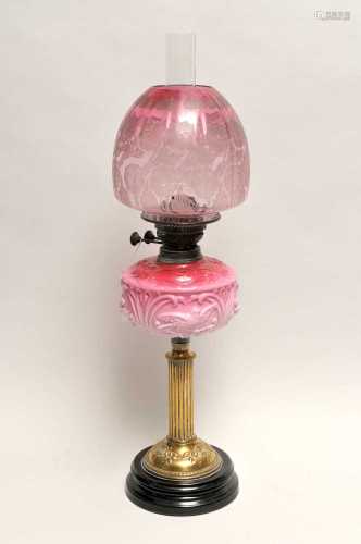 A Victorian oil lamp, with a fluted brass column supporting an opaque cranberry tinted glass