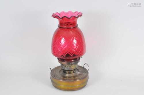 A large brass oil lamp, the cylindrical reservoir below a large pineapple-shaped cranberry glass