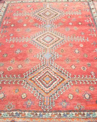 An old eastern woven wool rug, with a red ground and geometric medallions set within alternating