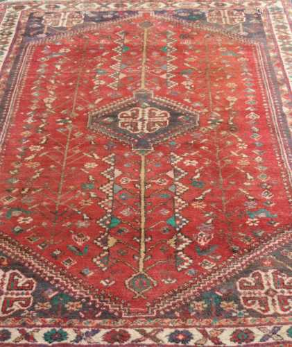 An old eastern woven wool rug, with a deep red ground decorated with symmetrical tree motifs, set