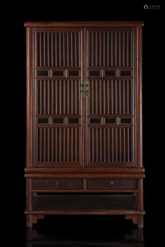 A hongmu wood cabinet on stand, the lower part with two drawers and a shelf, the upper part with slatted doors and sides, shelves inside China, 20th century (99x150x47 cm.)...
